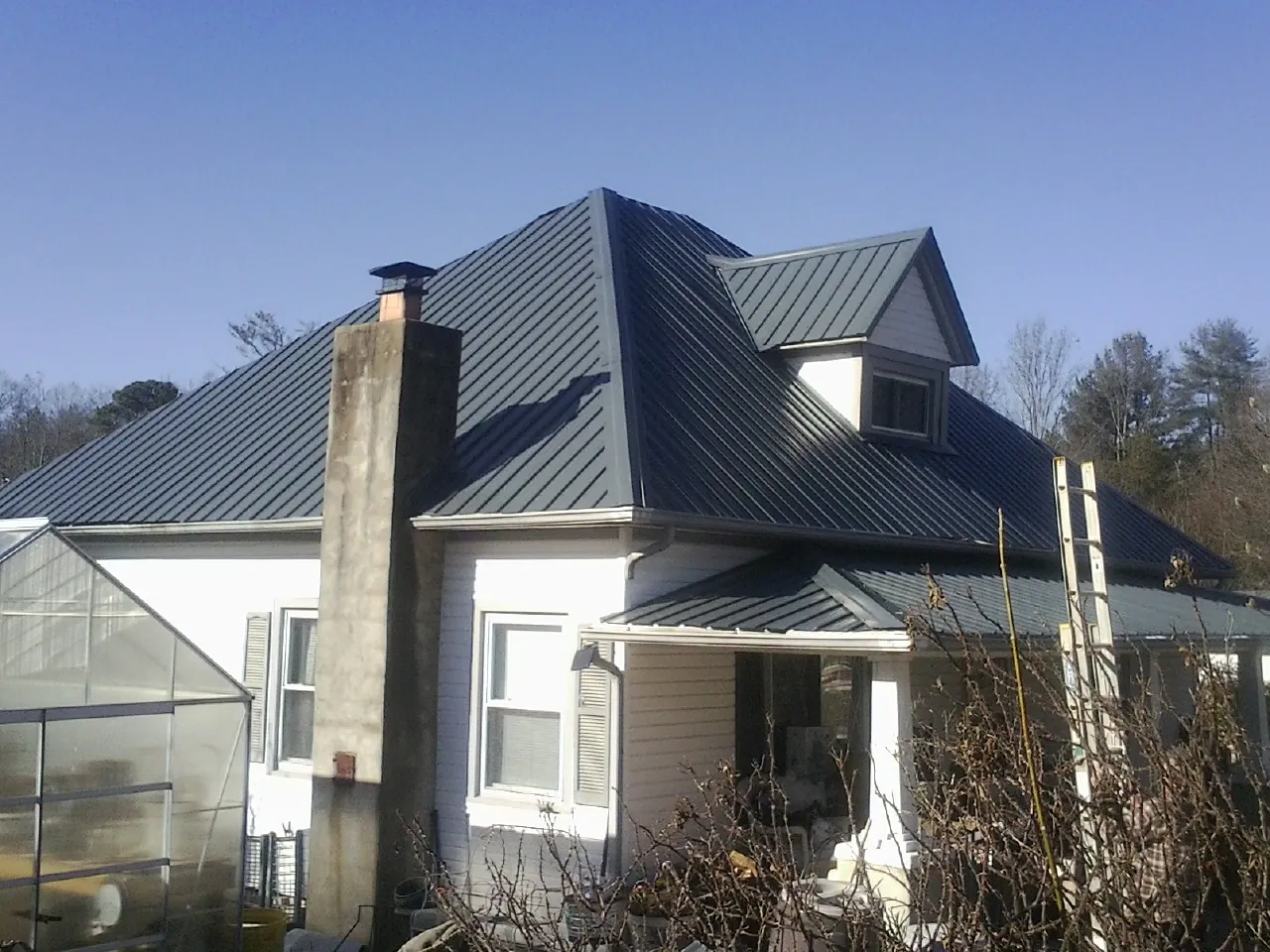 Dark blue standing seam metal roof on a white farmhouse with dormer — Slate & Tile Roof Repair by Roofing Brothers in Newhall