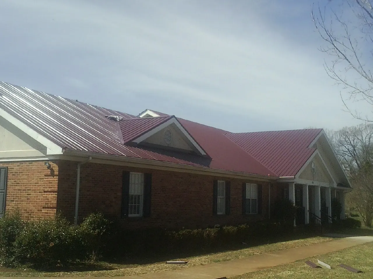 Red metal roof with gabled entries on a long brick building, from a Hail Damage Roof Repair job in Newhall